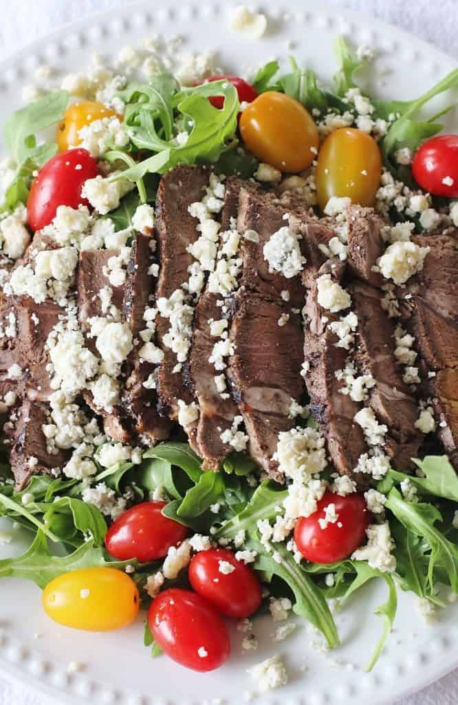 Sirloin Steak and Arugula Salad. Thinly sliced cold sirloin steak sits atop lightly dressed arugula. Cherry type tomatoes are added to the side and the blue cheese crumbles get sprinkled on top.