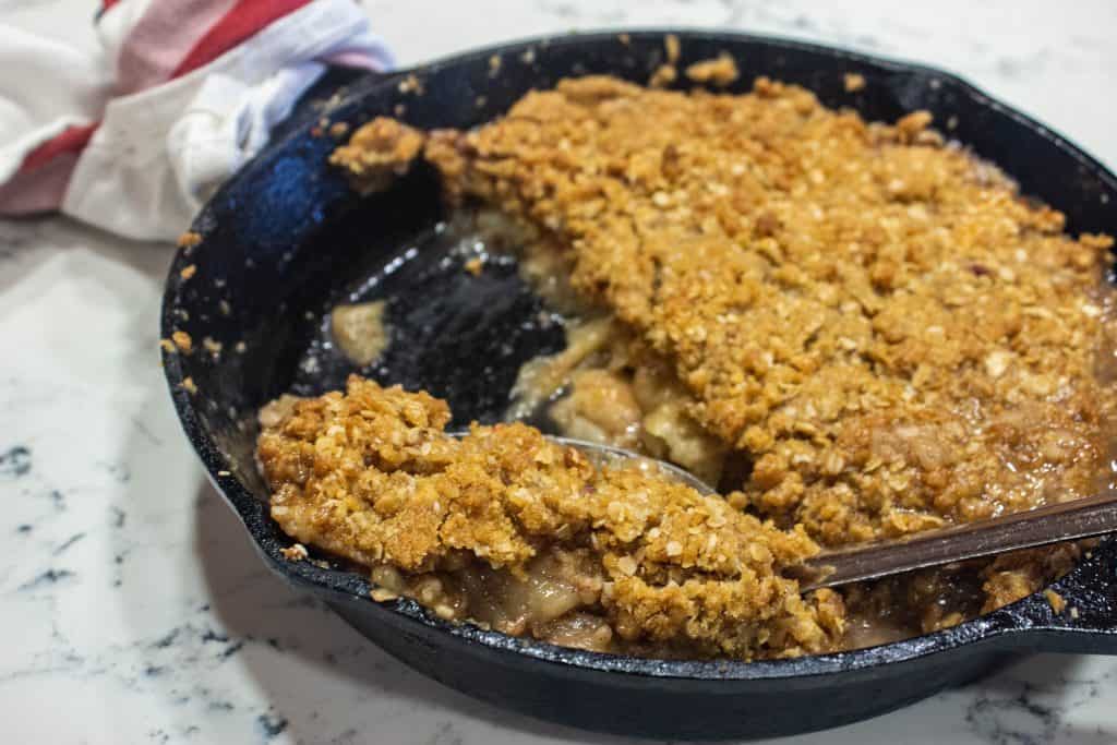 apple crisp in a cast iron skillet with a serving spoon